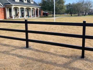 Black wooden fence in front of a house on dry grass.