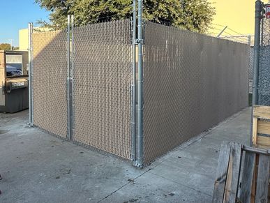 A fenced corner area with privacy screens on a concrete ground under the sunlight.