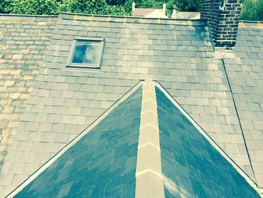 Slate roof with a skylight window and a brick chimney under a sunny sky.
