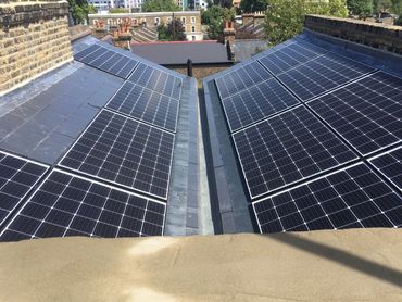 Solar panels installed on two sloped rooftops in an urban area.