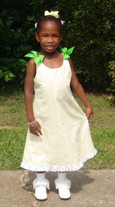 Young girl in a light yellow dress with green bows smiling outdoors.