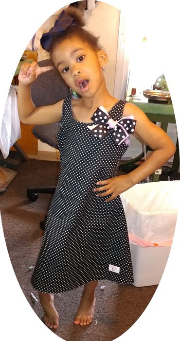 Young girl in a black and white polka dot dress striking a playful pose.