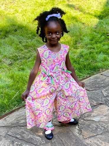 Young girl posing outdoors in a colorful patterned dresslotte with a white bow in her hair.