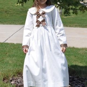 Young girl in a white dress with leopard print accents and matching hat.