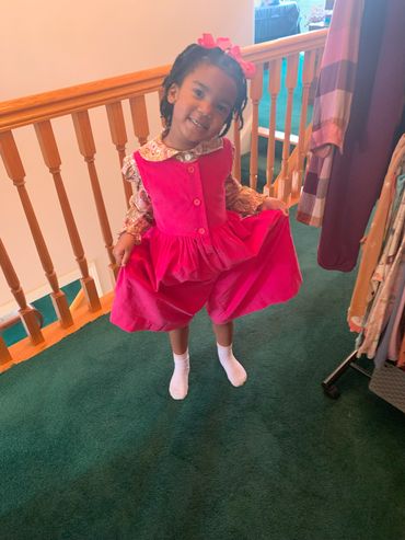 A smiling little girl in a bright pink dress posing indoors.