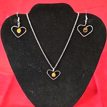 Heart-shaped silver necklace and earrings with amber beads on black display.