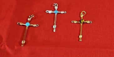 Three handmade cross pendants with colored stones on a red background.