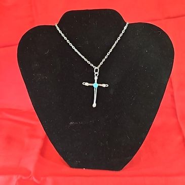 Silver cross necklace with turquoise inlay on black display against red background.