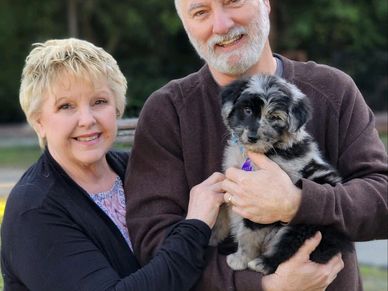 Elderly couple holding a small puppy outdoors.