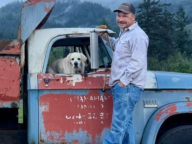 Man standing on doorsteps of an old dump truck outdoors.