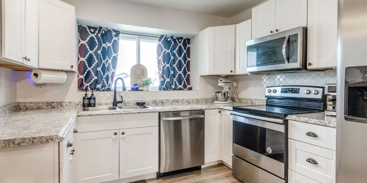 Bright modern kitchen with white cabinets, stainless steel appliances, and patterned curtains.