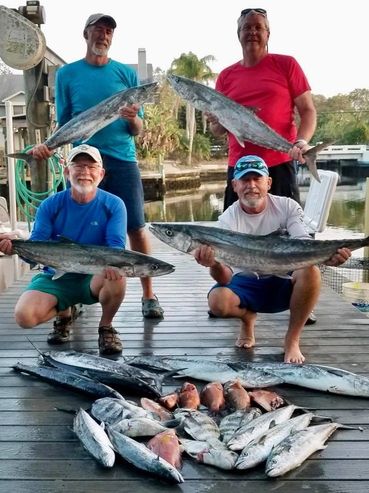 Four men proudly display their large fish catch on a dock by the water.