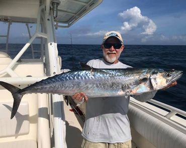 Man proudly holding a large fish on a boat in the ocean.