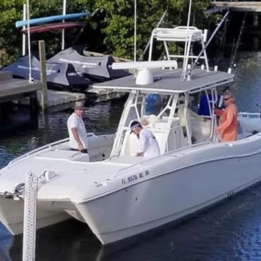 Three men on a white motorboat docked near jet skis in a marina.