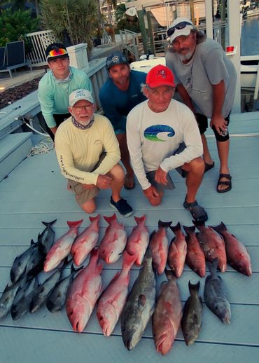 Five men pose with their fresh catch of various fish on a dock.
