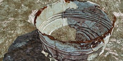 A rusty, worn metal bucket casting a shadow on a rough surface.