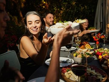 Friends happily sharing food at an outdoor dinner party with warm lighting.