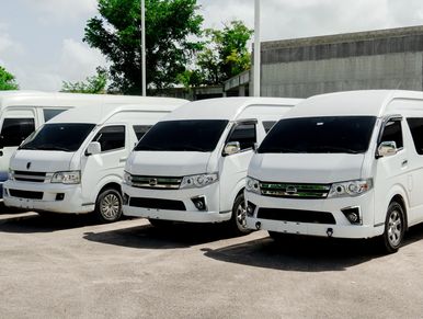 Four white passenger vans parked side by side on a sunny day.