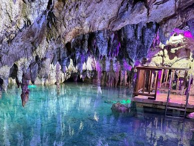 Crystal-clear water and stalactites inside a beautifully lit cave pool.