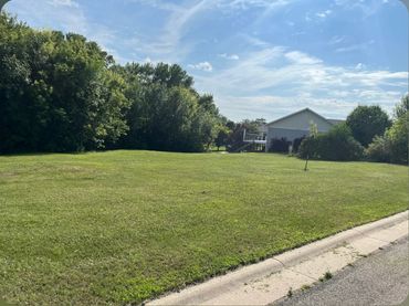 Open grassy yard with trees and a house under a partly cloudy sky.