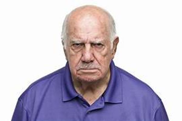 Elderly man in purple shirt with a stern expression.