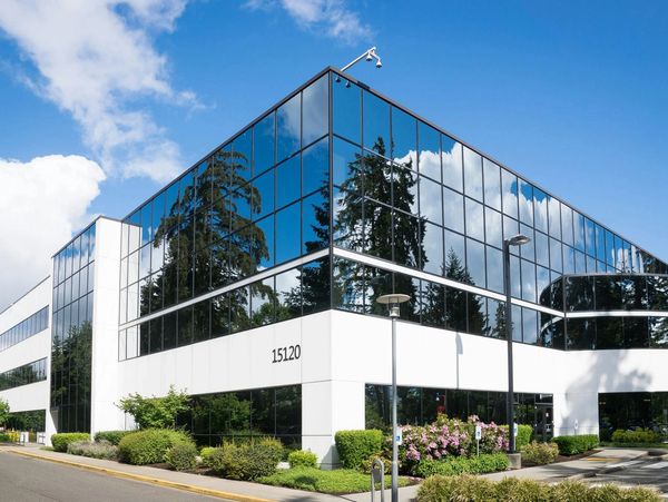 Modern office building with reflective glass windows and white walls under a clear blue sky.