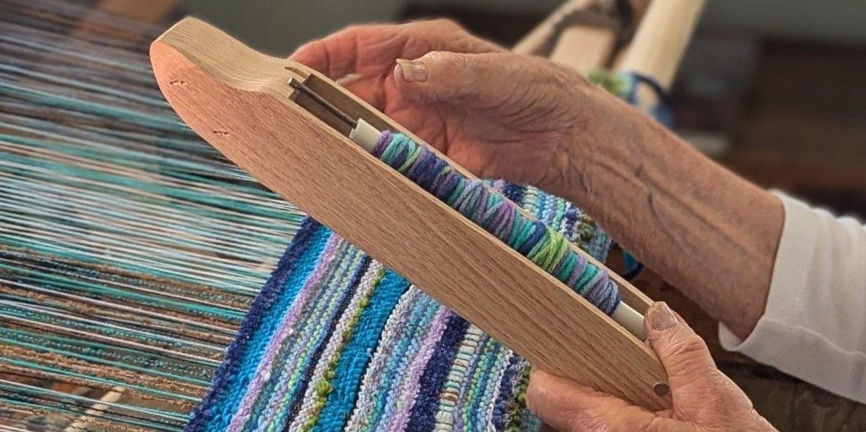 Elderly hands weaving colorful fabric on a loom with a wooden shuttle.