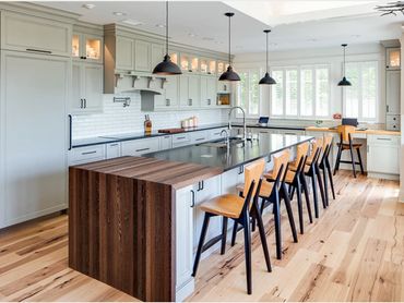Spacious modern kitchen with a large island, wooden stools, and pendant lights.
