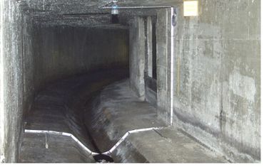 Dimly lit concrete tunnel with a narrow water channel inside.