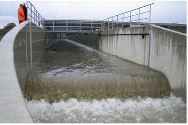 Water flows forcefully through a concrete flood channel with a person observing.