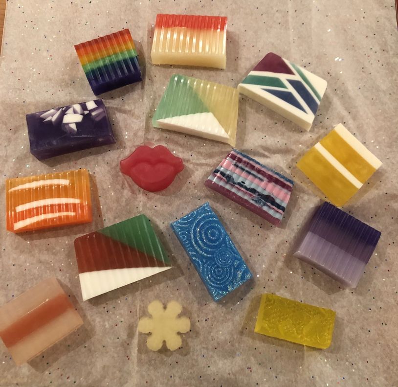 Colorful handmade soaps with various designs on a sparkly surface.