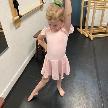 A young girl in a pink ballet outfit poses in a dance studio.