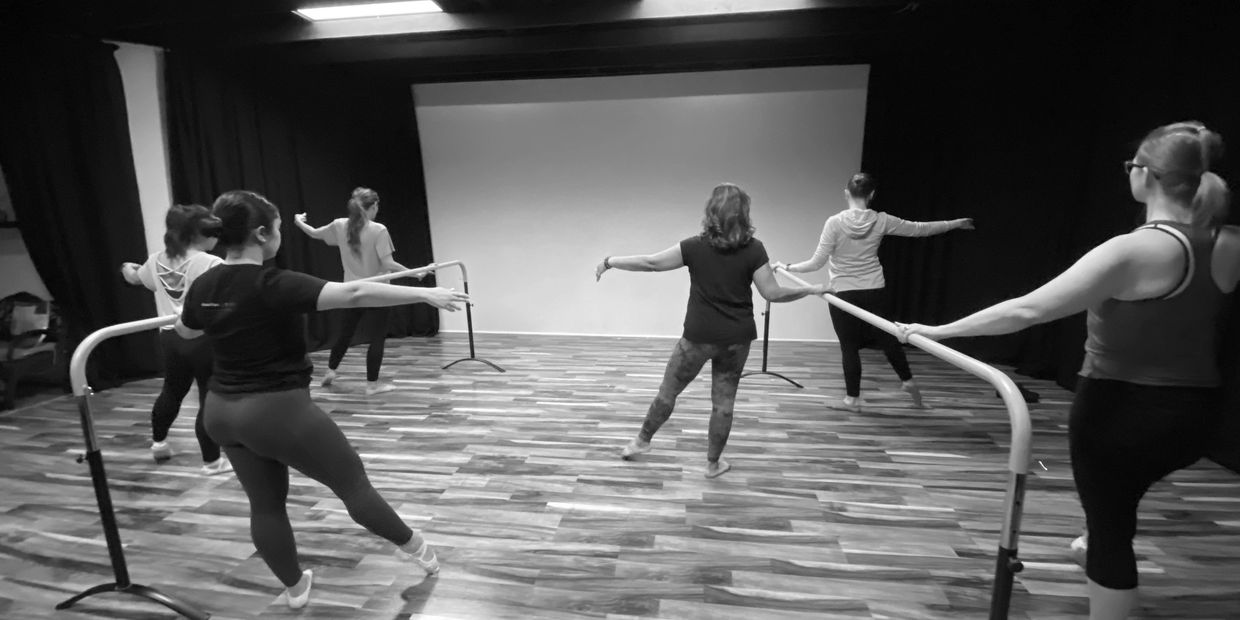A group of women practicing ballet at a dance barre in a studio.