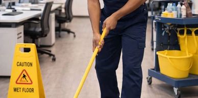A janitor mopping the floor in a clean office space with caution sign nearby.
