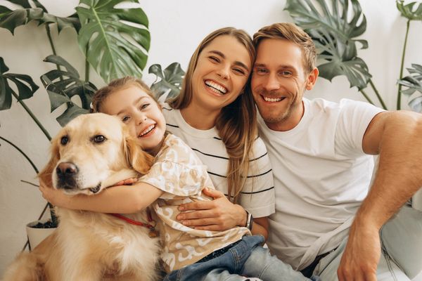 Happy family sitting on floor with young daughter and brown dog in living room