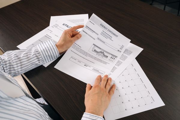 Hands reviewing an energy statement and other documents on a dark desk.