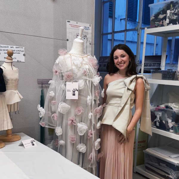 Happy woman posing next to a floral dress on a mannequin in a studio.