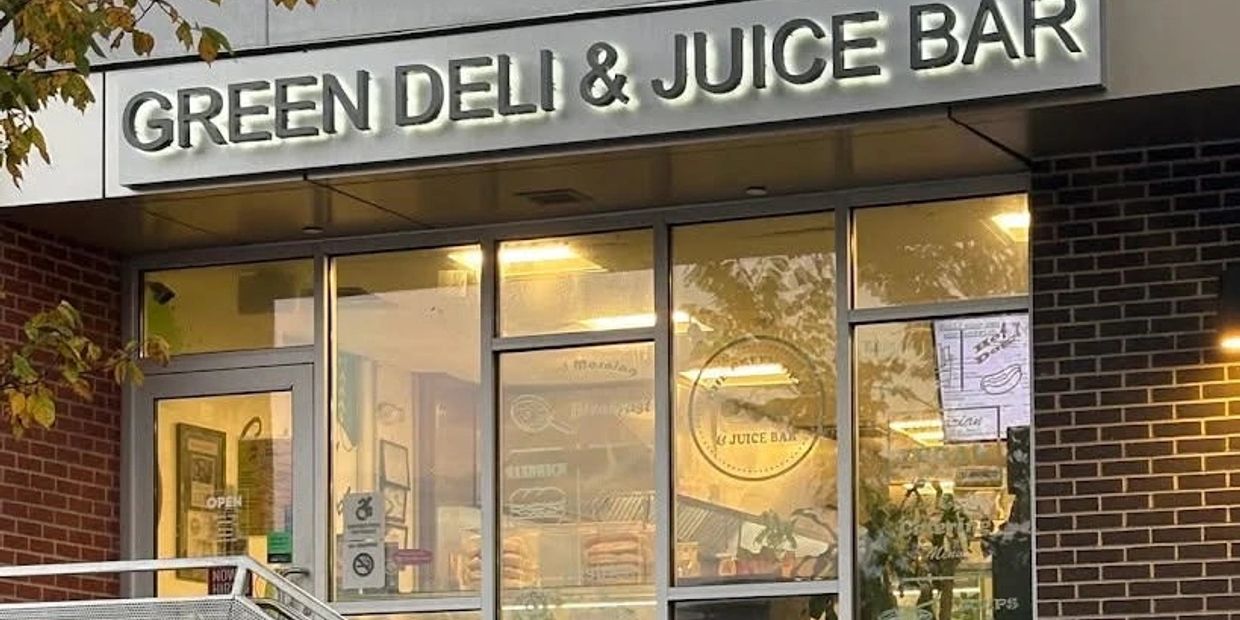Fachada del Green Deli & Juice Bar con luces encendidas.
