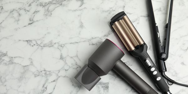 A hairdryer hair tongs and hairwavers on marble background