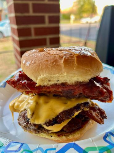 A bacon cheeseburger is sitting on top of a paper plate.