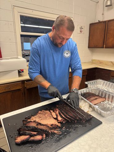 A man in blue shirt slicing meat on top of a black tray.