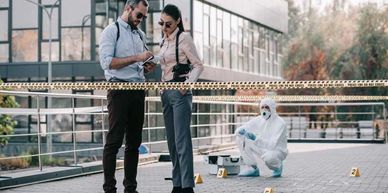 Detectives and forensic expert investigating an outdoor crime scene with evidence markers and police tape.