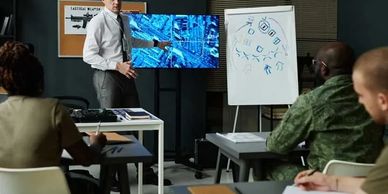 Man presenting tactical strategy to military personnel in a classroom.