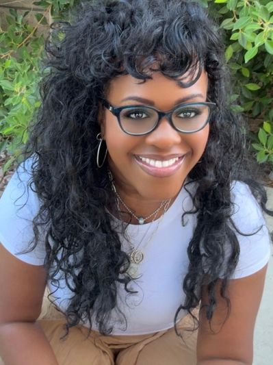 Smiling woman with curly hair and glasses outdoors near greenery with All Minds Clear.