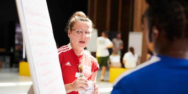 A woman in a red shirt teaching or presenting to a group indoors.