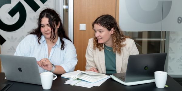 Two women collaborating with laptops and documents in a modern office.