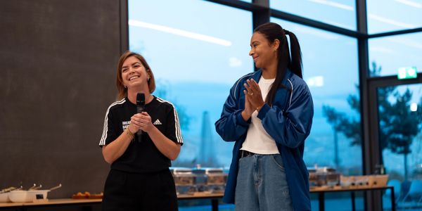 Two women smiling and speaking with a microphone at an indoor event.