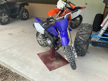 Two dirt bikes, one blue and one orange, parked in a garage.