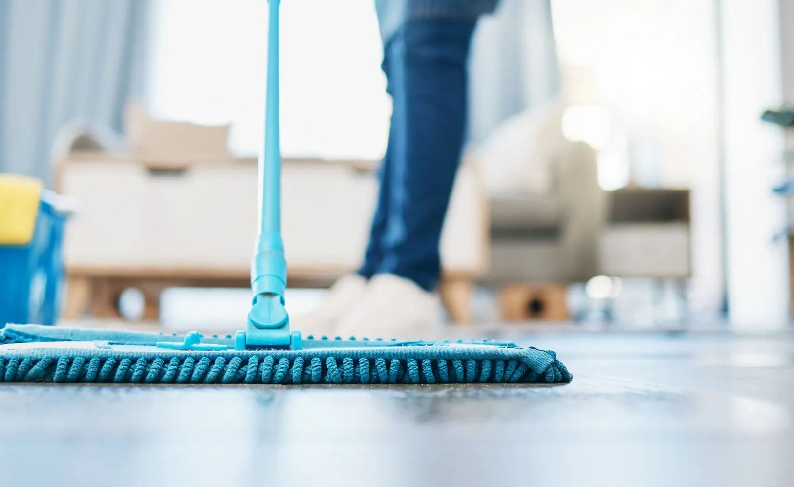 Person wearing yellow gloves moping floor with a green duster