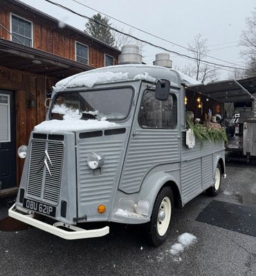Vintage Citroën van with snow on the roof, parked outside a wooden building.